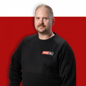 Mies mustassa paidassa, seisoo punaisen taustan edessä.