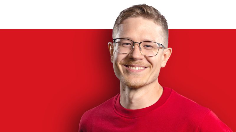A young man in a red shirt smiles against a white and red background.